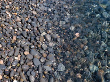 Bir çakıl taşı plajının yüzeyi ve berrak deniz suyu dalgaları.