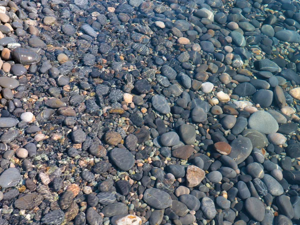 Bir çakıl taşı plajının yüzeyi ve berrak deniz suyu dalgaları.