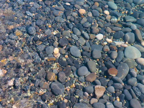 Bir çakıl taşı plajının yüzeyi ve berrak deniz suyu dalgaları.