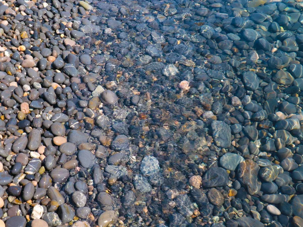 Bir çakıl taşı plajının yüzeyi ve berrak deniz suyu dalgaları.