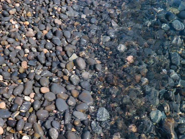 Bir çakıl taşı plajının yüzeyi ve berrak deniz suyu dalgaları.