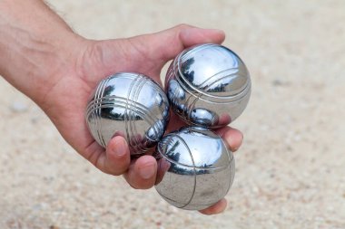 El, tipik bir Fransız oyunu olan Jeu de Boule 'u oynamak için üç Bocca topu tutuyor.