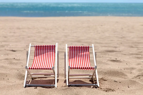阳光明媚的日子 在海边有两把带条纹的海滩椅子 图库图片