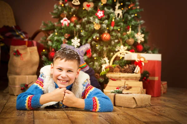 Christmas Child under Xmas Tree, Happy Boy Kid lying on wood floor front of New Year Presents Gifts
