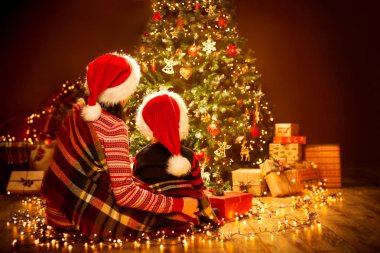 Noel aile geri arka görünümü Xmas ağacı, anne ve çocuk kırmızı Santa şapka oturan isteyen