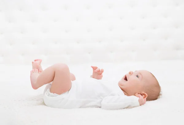 Baby auf weißem Bett liegend, glücklich lächelndes Kleinkind, lustiger Junge — Stockfoto