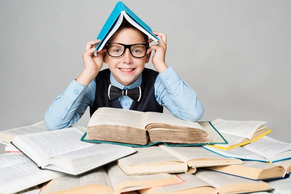 Niño feliz leyendo muchos libros con el libro en la cabeza, niño divertido de la escuela —  Fotos de Stock