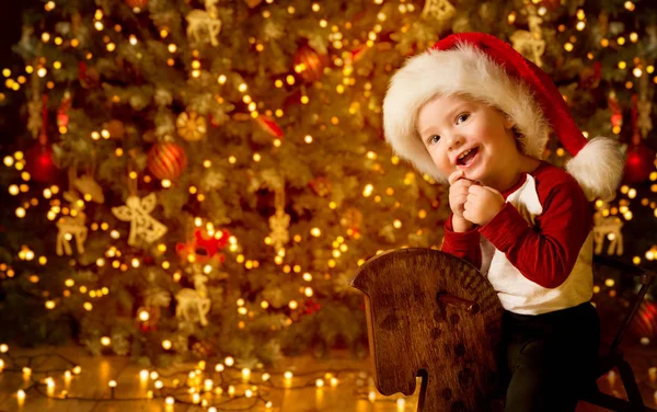 Glückliches Kind vor der Weihnachtsbeleuchtung, glückliches Baby mit roter Weihnachtsmütze — Stockfoto