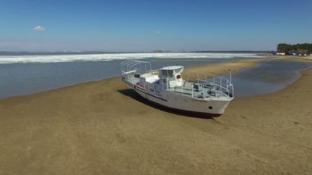 ロシア シベリアの寒い春の天気の中に凍った海水面の空中ドローン ショット 白い船と砂浜の上飛んでいます 砂浜にボートをクルーズします — ストック動画