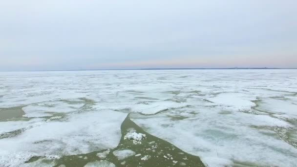 ロシア シベリアの寒い春の天気の中に凍った海水面の空中ドローン ショット 砂浜の上を飛んで氷の流氷と夕日をそれらの間の亀裂を氷 — ストック動画