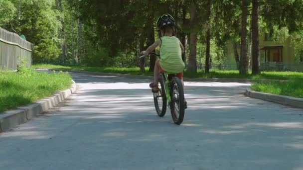 幸せな子外私道に自転車を駆動するための学習します 少年ヘルメットを身に着けている郊外にアスファルトの道路で自転車に乗る スローモーション — ストック動画