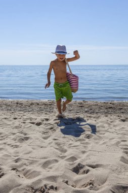 Plaj çantası yaz tatilde çocukla. Mutlu çocuk güzel deniz, doğayla çalışan kum ve mavi gökyüzü. 