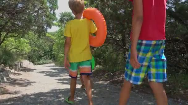 带充气圆圈的儿童沿着风景如画的瞻博树丛中的海滩小径漫步 — 图库视频影像