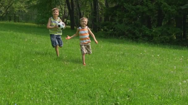 happy kids running with a soccer ball on green grass in sunny day. Slow motion.