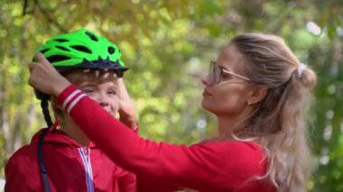 anne oğluna yardım yeşil Bisiklet kask sonbahar parkta giyer.