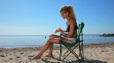 Genç kadın plajda, güneşli havalarda sandalye üzerinde oturan güneş koruyucu losyon uygulamak