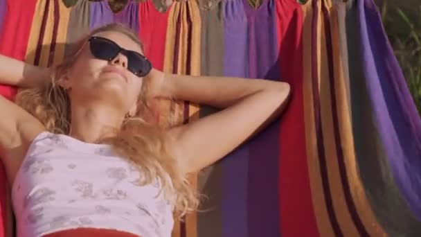 年轻美丽的女孩戴着太阳镜躺在吊床上 美丽的女人 金发碧眼的休息度假 — 图库视频影像