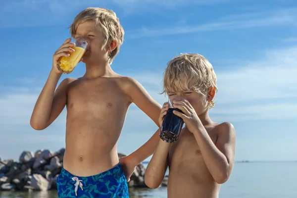 两个男孩在海边阳光明媚的日子放松和喝果汁 — 图库照片