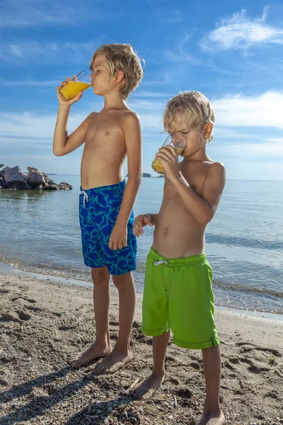 孩子们站在沙盘上 在炎热的夏日喝橙汁 — 图库照片