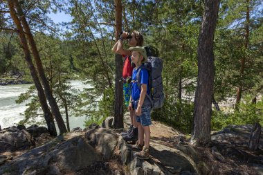 Sırt çantası olan çocuklar dürbünden bakıyor. Dağlarda yürüyüş eden çocuklar. Aktif seyahat kavramı.