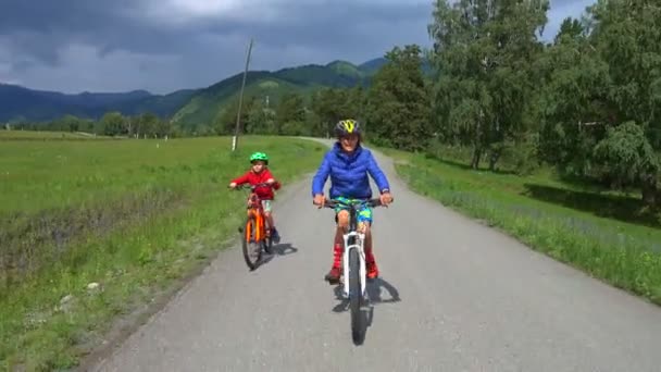 田舎道で自転車に乗る2人の幸せな子供たち 森と山と美しい自然 — ストック動画