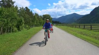 Dağlarda yolda bisiklete binen mutlu çocuklar, beyaz bulutlarla mavi gökyüzü. Güzel yaz günü.