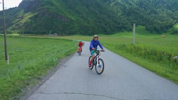 Meninos Felizes Andando Bicicleta Estrada Montanhas Vacas Pastando Prado Perto — Vídeo de Stock