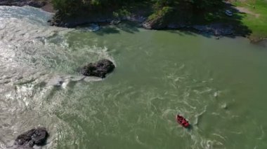 Dağ Nehri'nde kırmızı rafting teknesinin havadan çekilmiş fotoğrafı. Rafting ekibi suya sıçrayan kürekler ile rapids inen. 