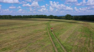 Havadan görünüm: Çocuk alanında yalnız bir yolda bisiklete biniyor. Bulutlu gökyüzü ile güzel doğa.