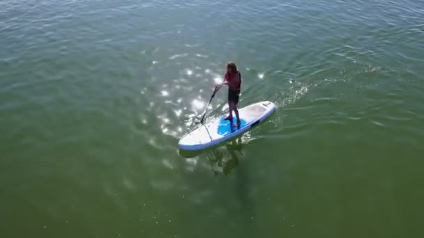 休暇中にパドリングをする少年の空中写真 太陽のまぶしさで川に浮かぶ少年サップ搭乗 — ストック動画