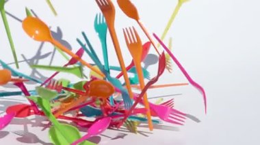 Beyaz arka planda yavaş çekimde düşen çok renkli plastik çatal ve kaşıklar