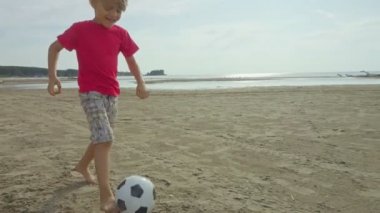 İki mutlu çocuk plajda koşup futbol oynuyorlar, ağır çekimde.