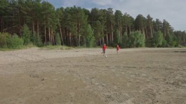Çocuklar çocuklar runnung ve orman yakınındaki plajda futbol topu tekme, futbol yavaş hareket oynarken