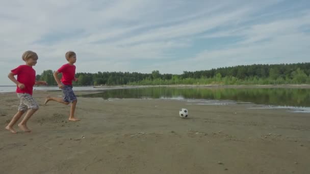 2人の幸せな男の子が走り ビーチの水にサッカーボールを蹴る スローモーション — ストック動画