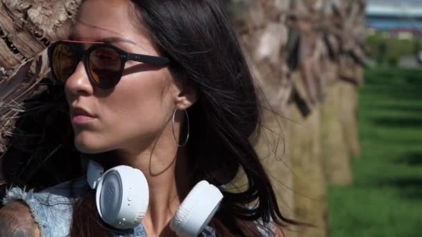 Jolie jeune femme brune hipster triste portant des lunettes de soleil fantaisie regarde autour par une journée ensoleillée — Video