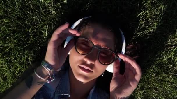 Närbild på asiatisk flicka tar av hennes solglasögon liggande på det gröna färska gräset — Stockvideo