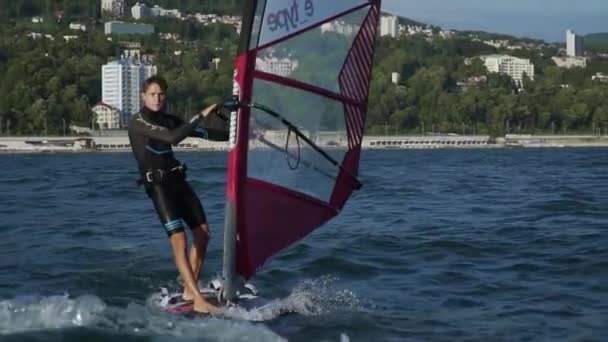 快活ハンサムな水スポーツマンは滑空水です。若い男は、休暇を楽しみます。水のエンターテイメント サービス。男性に乗って夕日の輝きの windfoil. — ストック動画