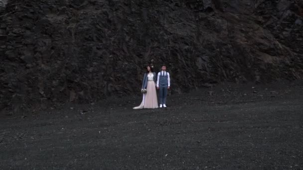 新娘和新郎在对比黑暗的岩石面前 新婚夫妇牵手 同时转身互相看 月亮的风景 户外婚礼仪式 威尔士安德森风格 — 图库视频影像