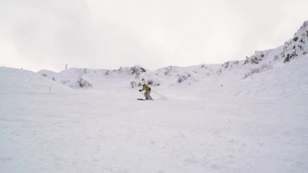 Esquiador vestido com roupas brilhantes faz ondas de neve e joga neve na câmera. Mulher esquiador passeios em uma colina de esqui vazio . — Vídeo de Stock