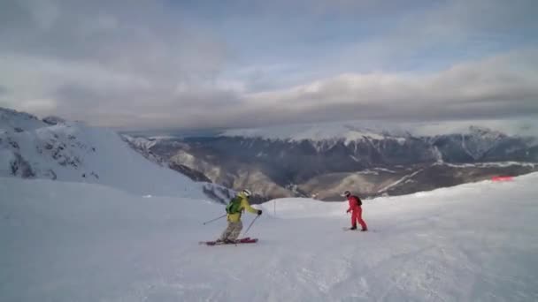 Лыжник и сноубордист спускаются с холма. Сноубордист в оранжевой одежде едет на пустой лыжной трассе . — стоковое видео