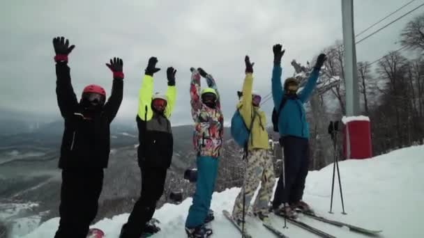 Grupo de esquiadores vestidos con cascos y equipos brillantes están uno por uno mirando a la cámara. Grupo de snowboarder poner manos arriba todos juntos. Los esquiadores están bailando muy divertido en conjunto . — Vídeos de Stock