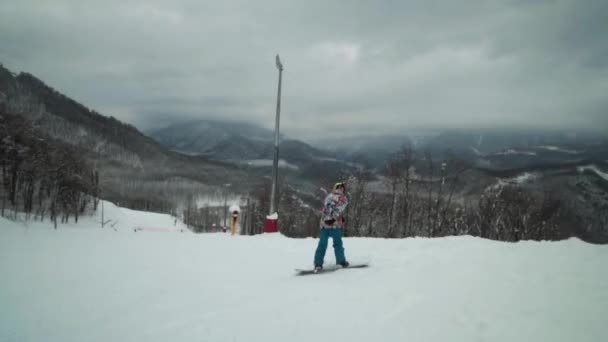 Acompanhe de perto um jovem snowboarder que está montando em uma pista de esqui vazia e enorme. Férias de inverno e aventuras na estância de esqui . — Vídeo de Stock