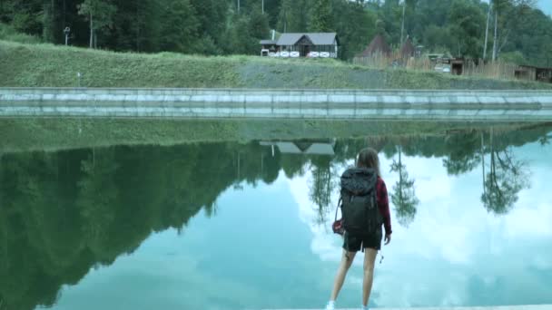 Mujer joven esportista vestida camisa a cuadros rojo tomada tiro de cuerpo completo que se divierte en la aventura de viaje de verano en la parte delantera del lago de montaña — Vídeo de stock