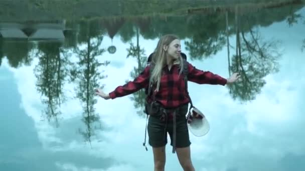 Sporty young cute lady with backpack explores nature summer travel adventure in the front of mountain lake — Stock Video