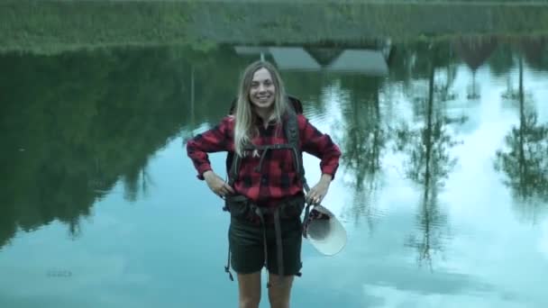 Csípő fiatal aranyos hölgy a hátizsák nevet, és mosoly ellen a kilép tükör felületének mountain-tó — Stock videók