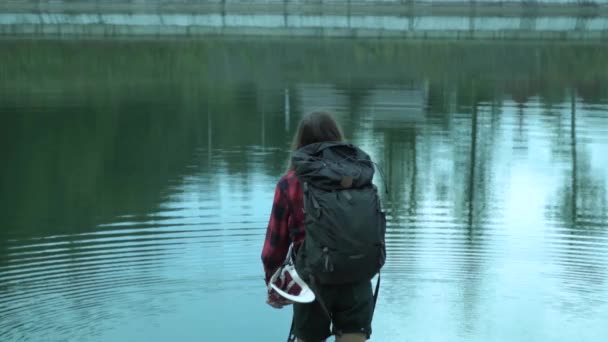 Movimiento lento de lanzar piedras al lago de montaña por la joven dama hipster mientras que la aventura — Vídeo de stock