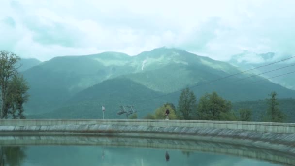 Pequeña figura de la señora excursionista y su maravilloso reflejo en la superficie del espejo de agua del lago contra los picos de verano fantásticos distantes y la vía de cable de esquí — Vídeo de stock