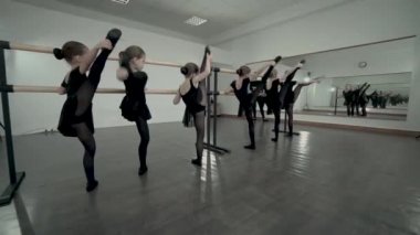 Siyah mayo giymiş küçük balerinler bir bacak yukarı alınan ile ayakta ve bale barre yakınında stetching egzersiz yapmak