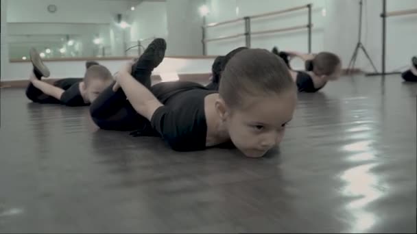 Close-up Retrato linda pequeña bailarina tumbada en el suelo en el estudio de baile y realizar el ejercicio de superman — Vídeo de stock