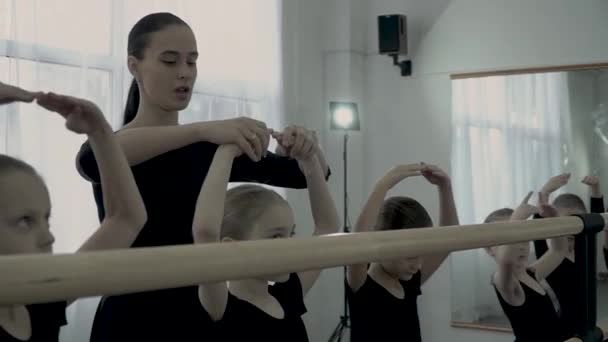 The strict female teacher of dance class correct position of little ballerinas and teach them how too keep hands up near ballet barre — Stock Video